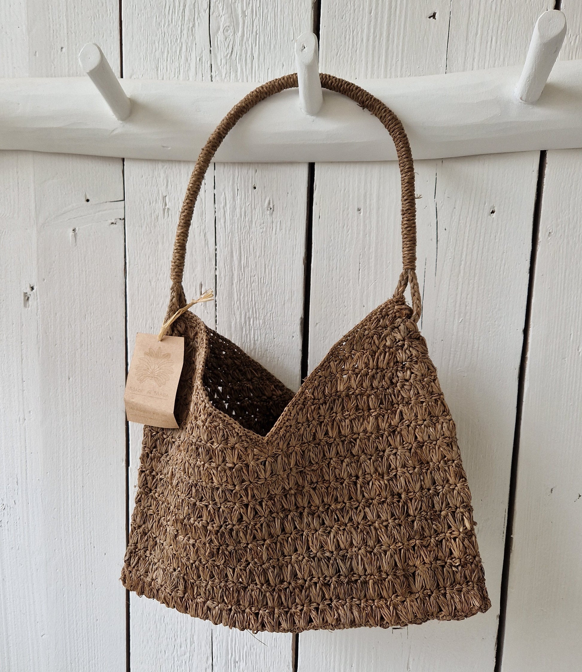 Valiha Bag van Made in Mada aan witte houten haak, handgeweven raffia tas met bohemian uitstraling en natuurlijk karakter