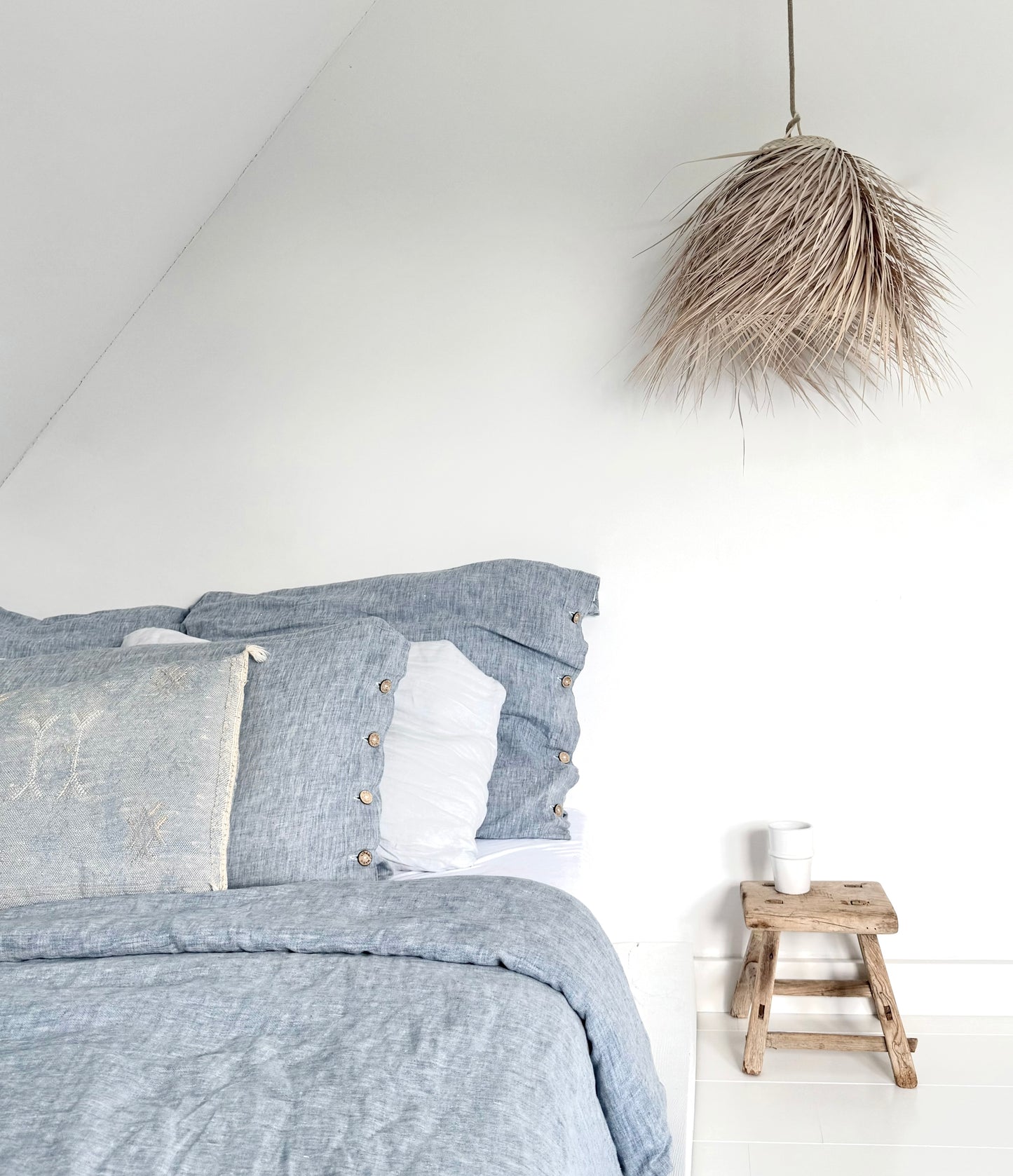 Palmleaf cloche lamp small boven bed met blauw linnen beddengoed