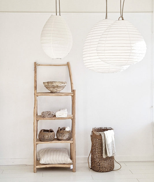 Wit interieur met katoenen lampion lampen, houten open kast en natuurlijke woonaccessoires.