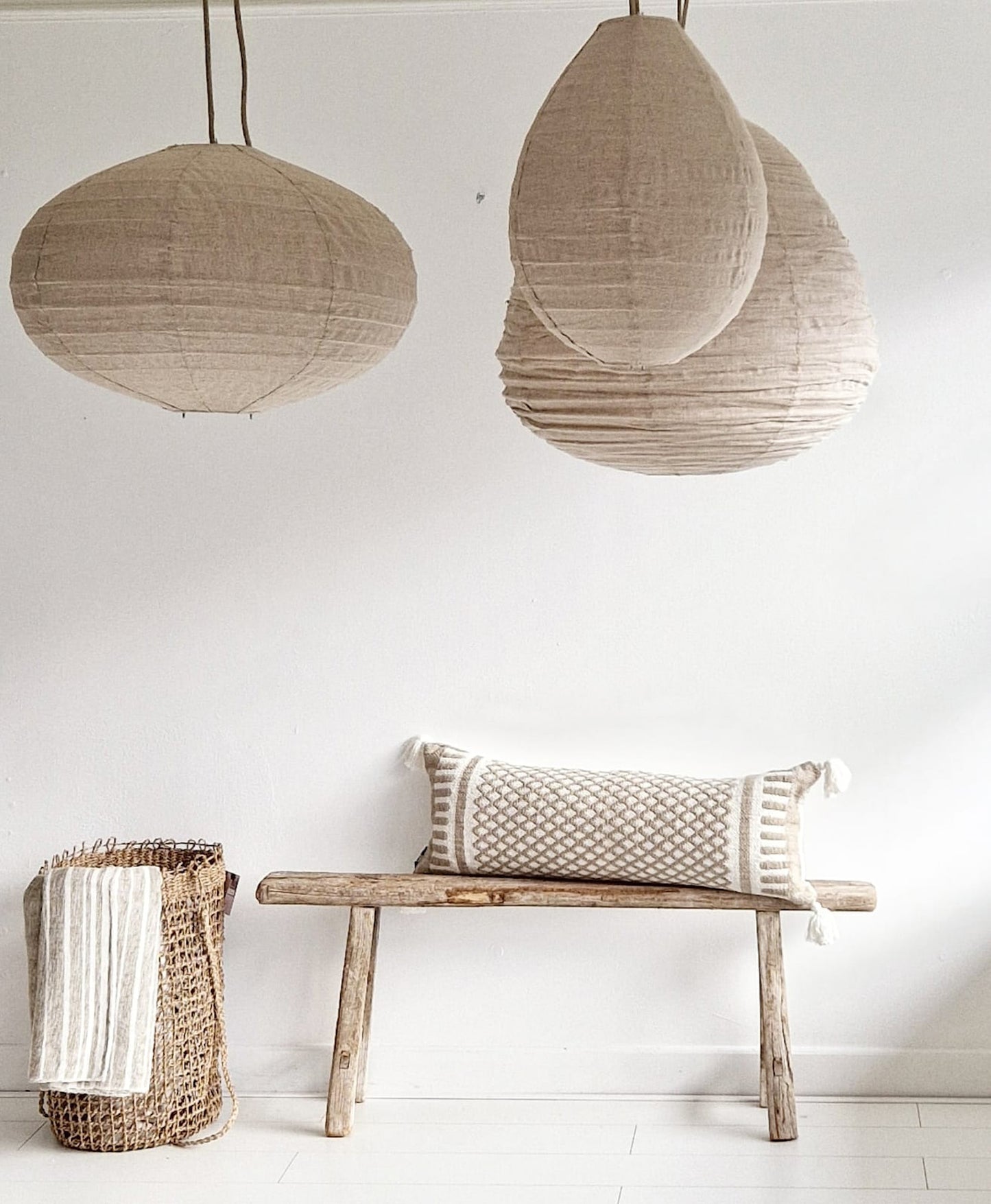 Wit interieur met drie linnen lampion hanglampen in naturel kleur boven een houten bank