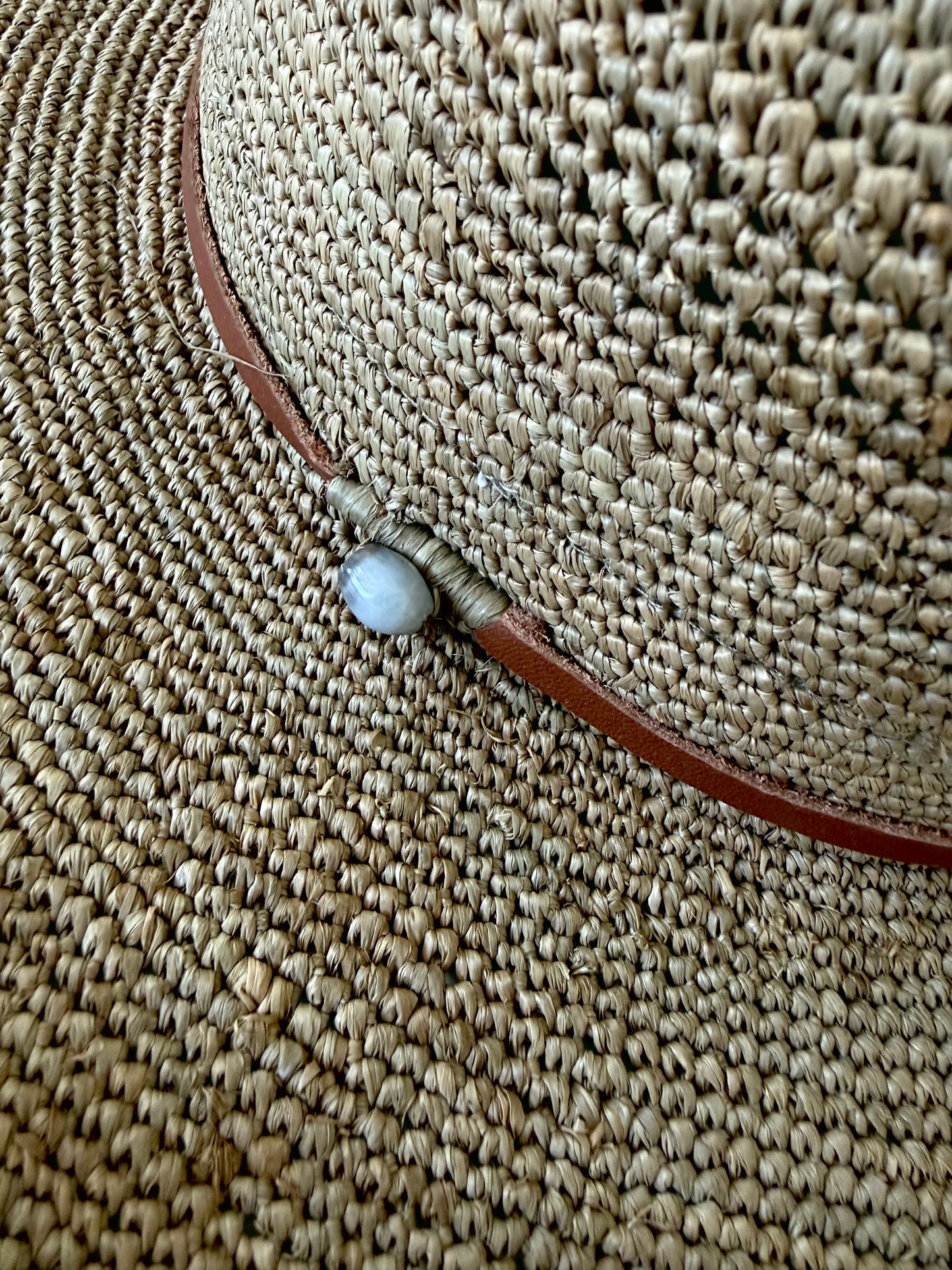 Close-up of the handwoven raffia texture and tan leather cord of the Aziz Hat by Made in Mada