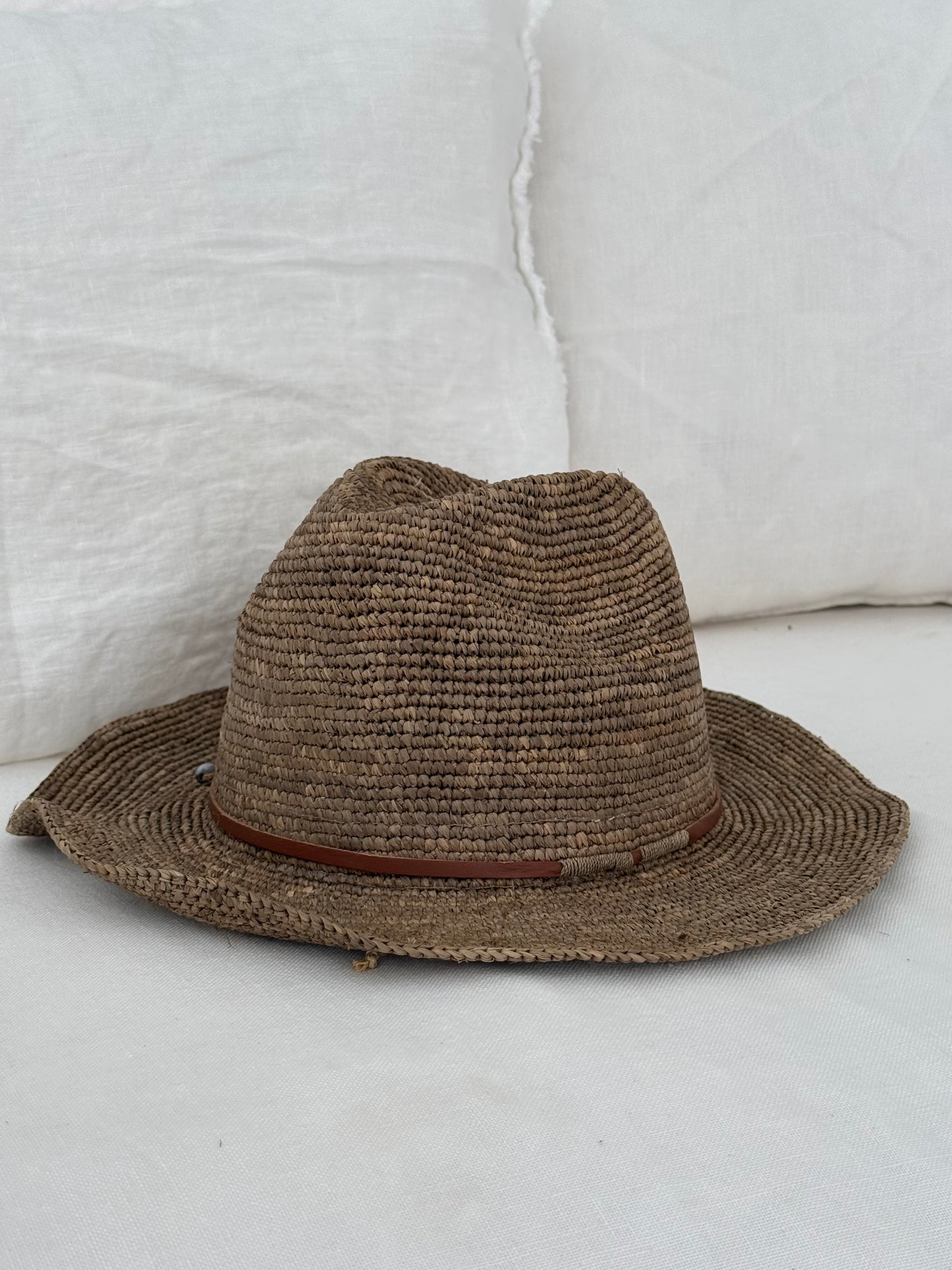 Raffia hoed Elya tan leather in tea kleur van Made in Mada op een witte linnen bank.