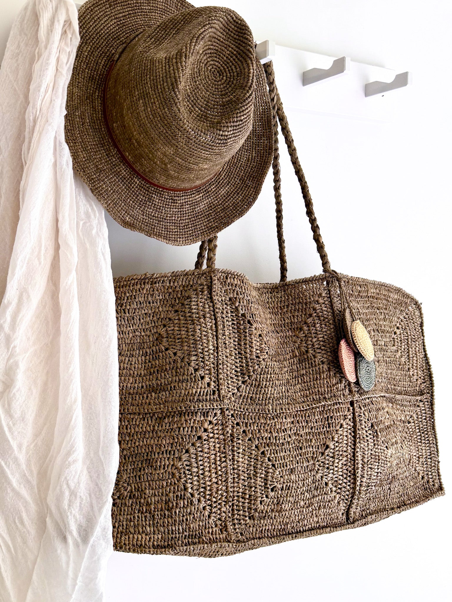 Raffia hoed Elya tan leather in tea kleur van Made in Mada aan een kapstok samen met de grote raffia Gaby bag in tea kleur van Made in Mada