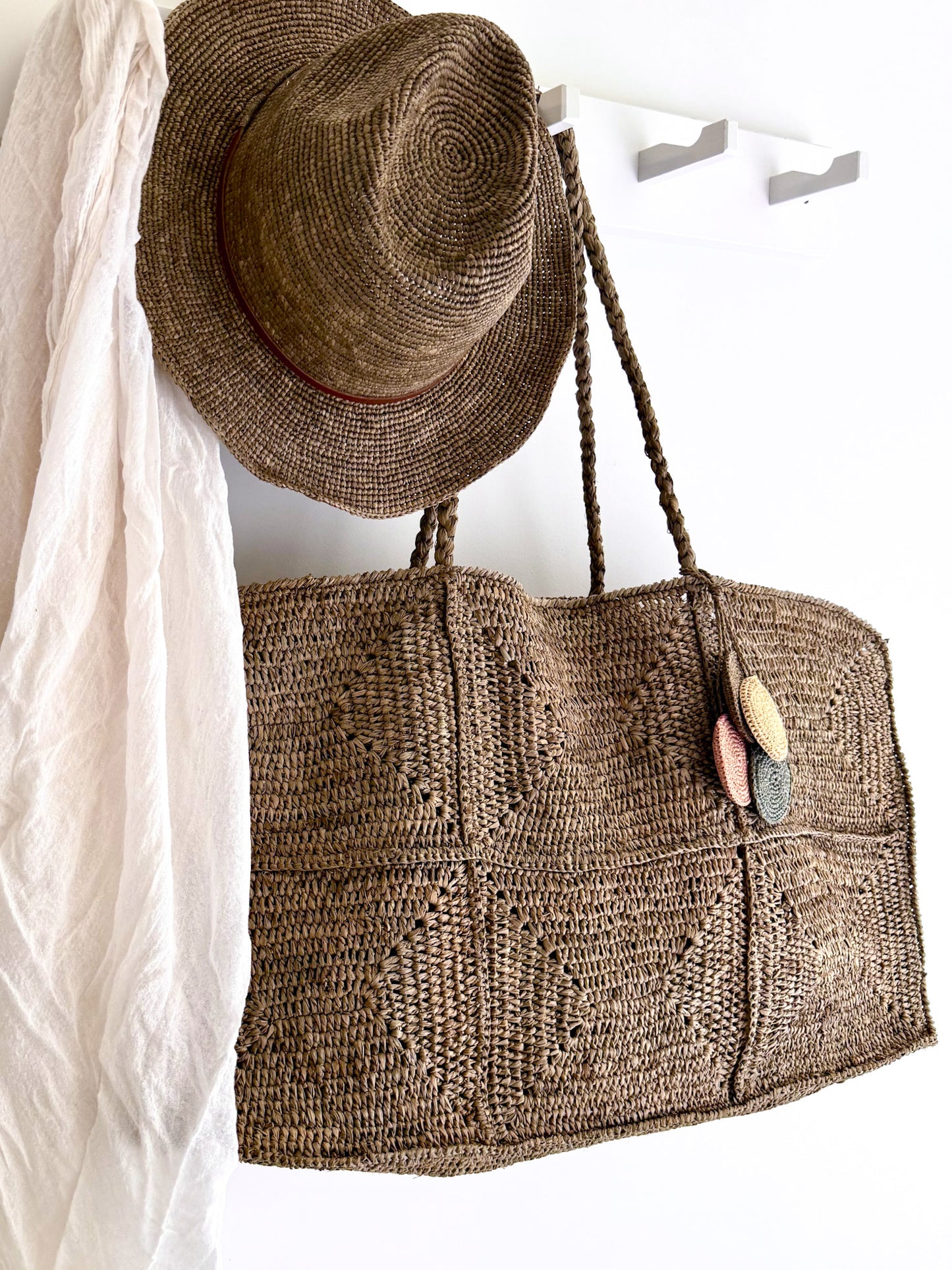 Grote Raffia tas Gabi en de Elya hat met tan leather in tea kleur van Made in Mada aan een kapstok.