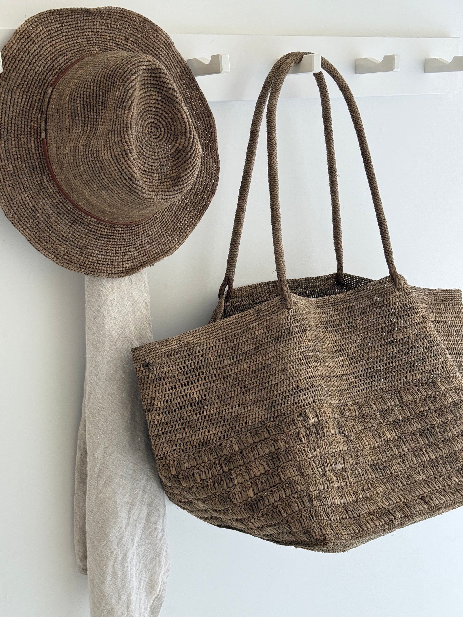 Raivo Bag Tea van Made in Mada grote raffia strandtas met binnenvak aan kapstok met raffia hoed Elya