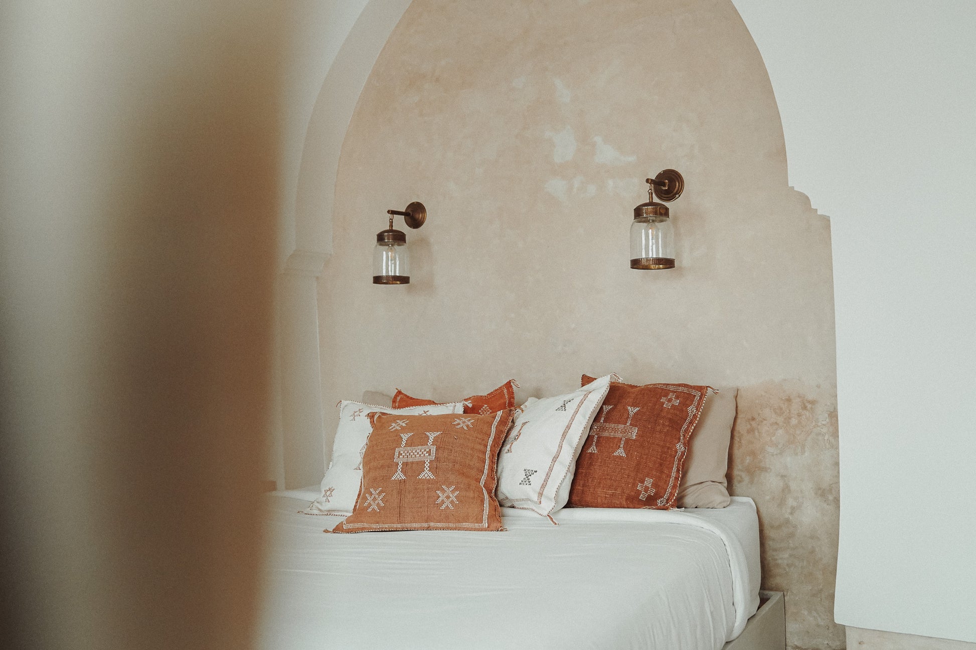 Meerdere Marokkaanse sabra silk kussens in off-white en bruin tinten op een bed in een Marokkaanse riad.