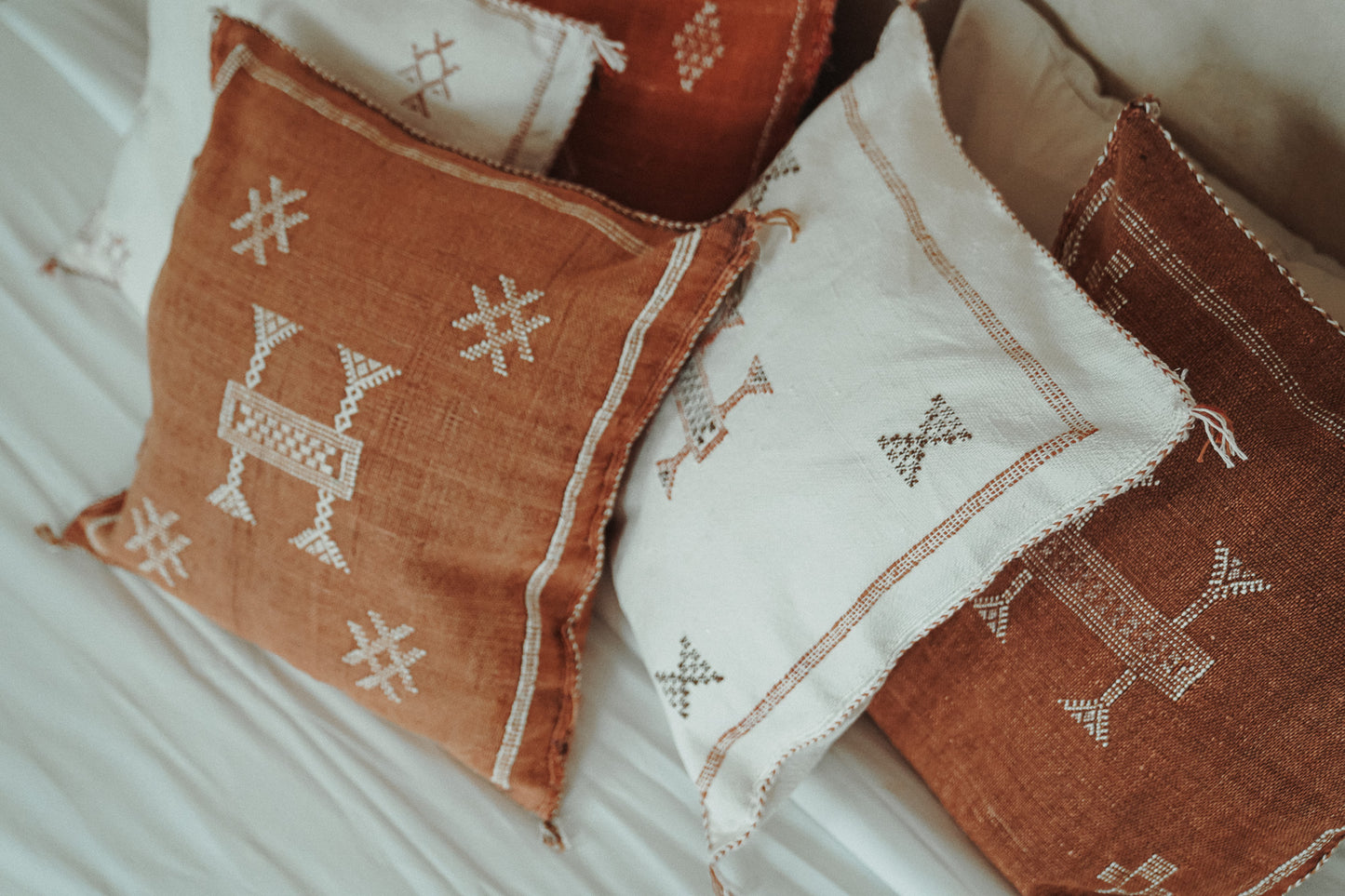 Meerdere Marokkaanse sabra silk kussens in off-white en bruin tinten op een bed