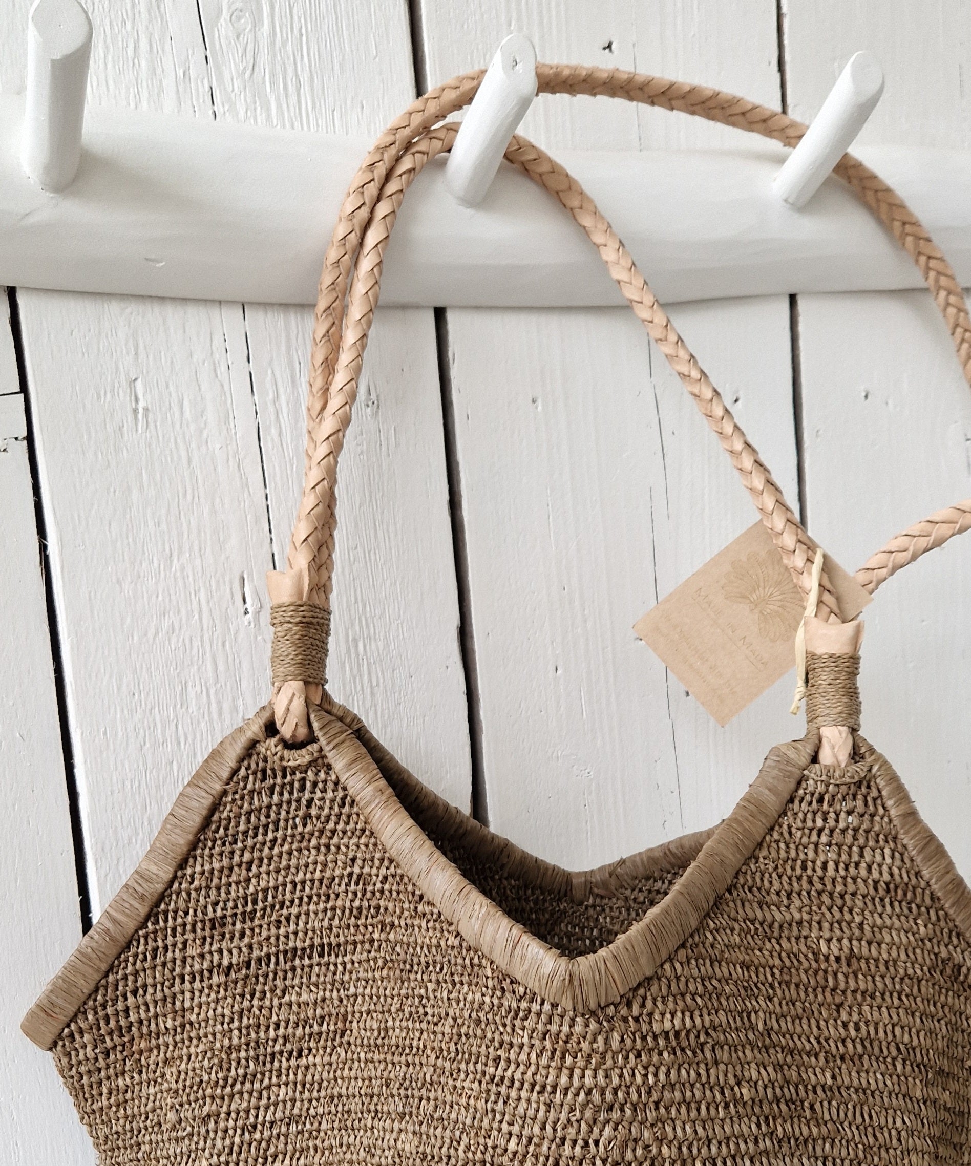 Close-up van gevlochten lederen hengsels van de Aina M Bag van Made in Mada, rustend aan witte houten kapstok