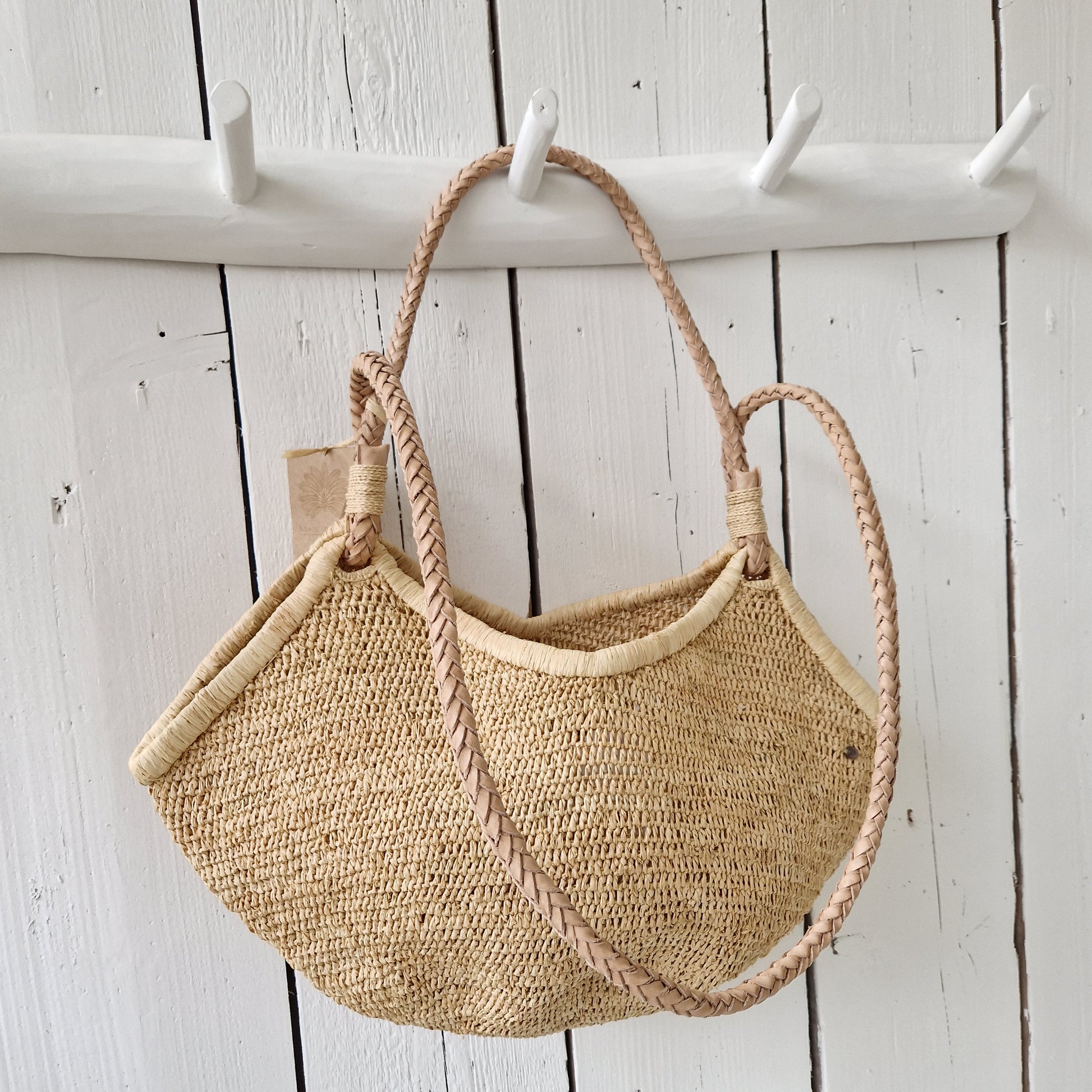 Aina M Bag Naturel van Made in Mada met gevlochten lederen hengsels, hangend aan witte houten kapstok