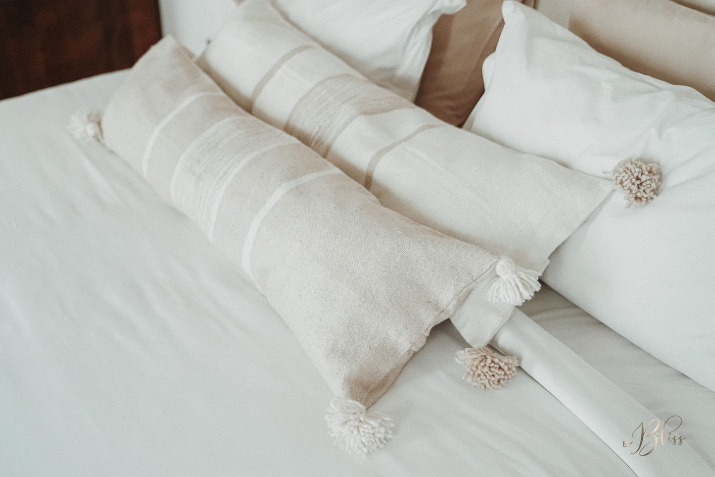 Marokkaanse pompom kussens beige en off-white op bed met wit linnengoed