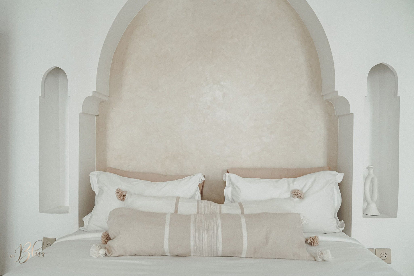 Marokkaanse pompom kussens beige en off-white in langwerpig formaat 30x100 op bed in een riad met een warm licht interieur