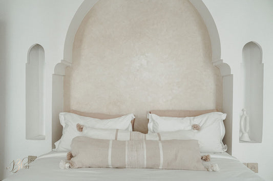 Marokkaanse pompom kussens beige en off-white in langwerpig formaat 30x100 op bed in een riad met een warm licht interieur