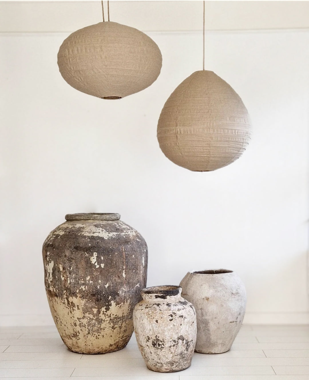 Sfeerbeeld met authentieke aardewerk potten in diverse maten en natuurlijke kleuren, gecombineerd met minimalistische linnen hanglampen in een lichte ruimte.
