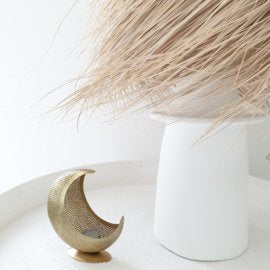 Witte Chakki tafel met een windlicht houder in de vorm van een goudkleurig maantje en daarnaast de palmleaf lamp N1 van Rock the Kashbah